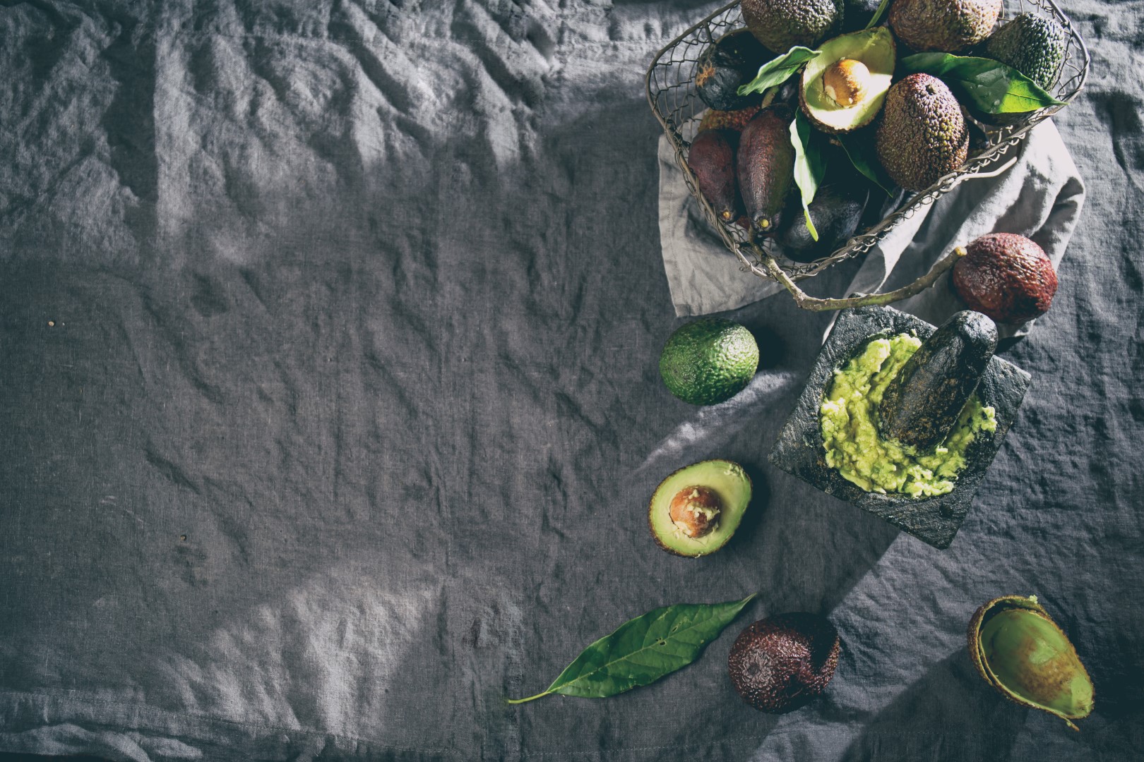 Avocado. Guacamole. Mexican guacamole sauce in stone mortar, full basket with avocado, half of avocado on linen tablecloth. Top view. Copy space.